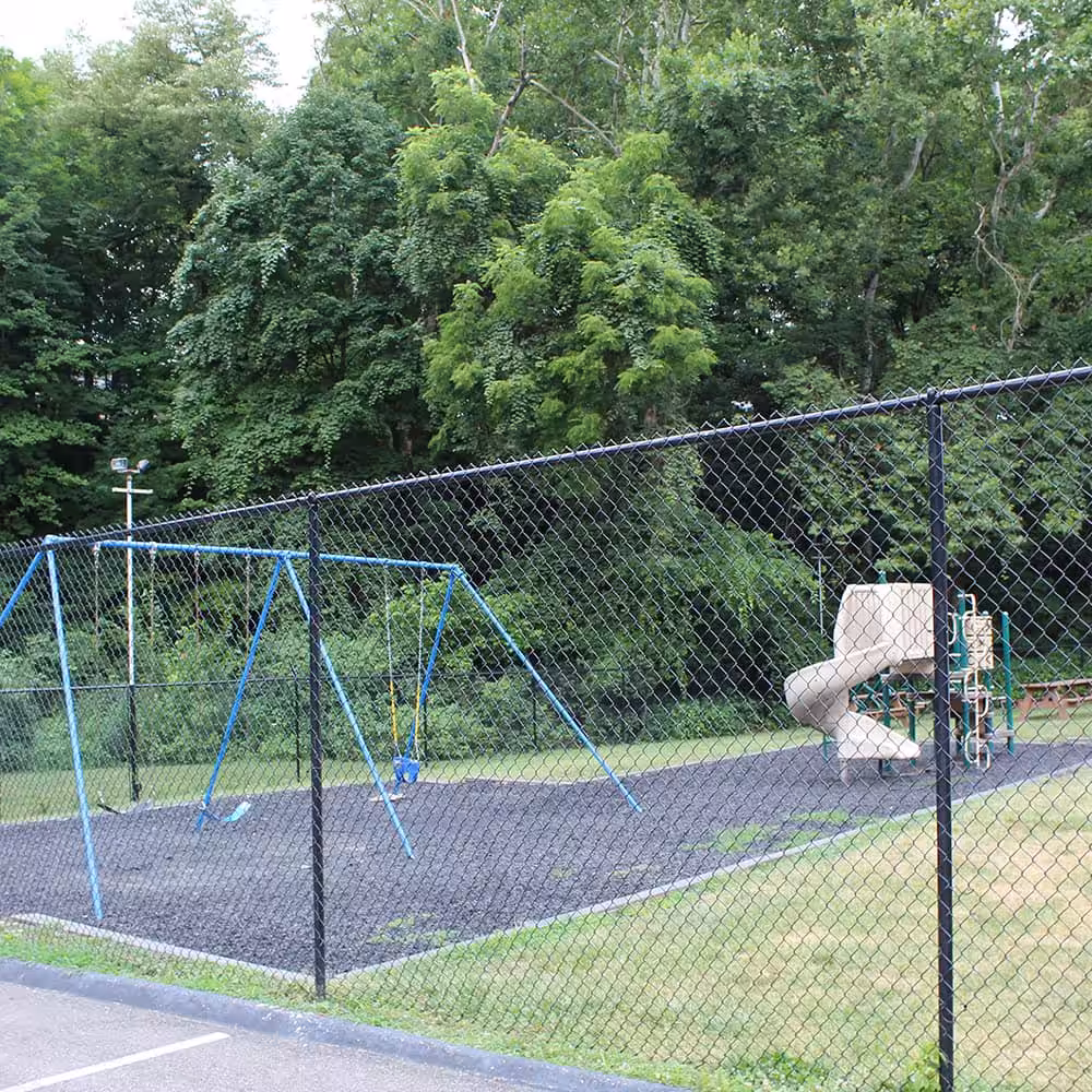 A chain link fence with a playground behind it