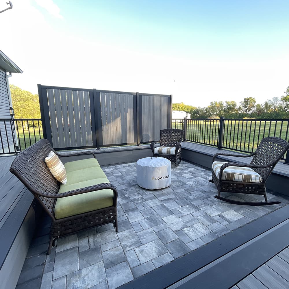 A concrete patio with a fire pit that a black fence with an amenity fence