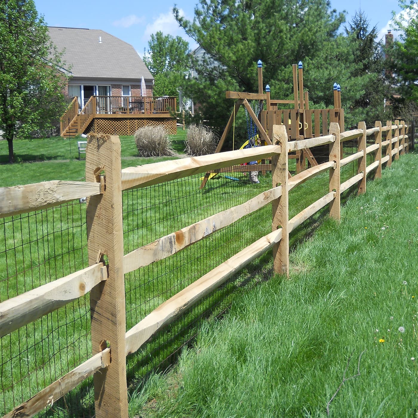 A split rail fence that is dividing two grass yards