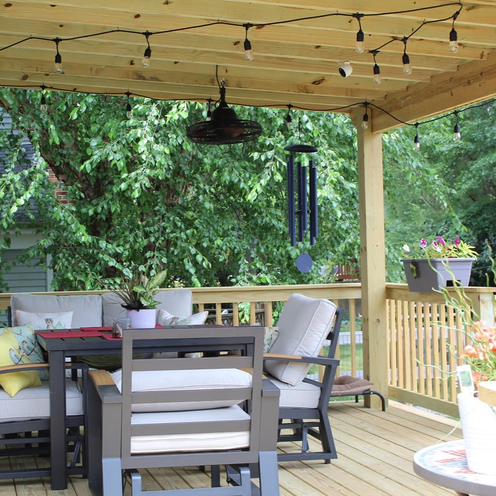 A wood deck with a wood roof that has lights hanging from it